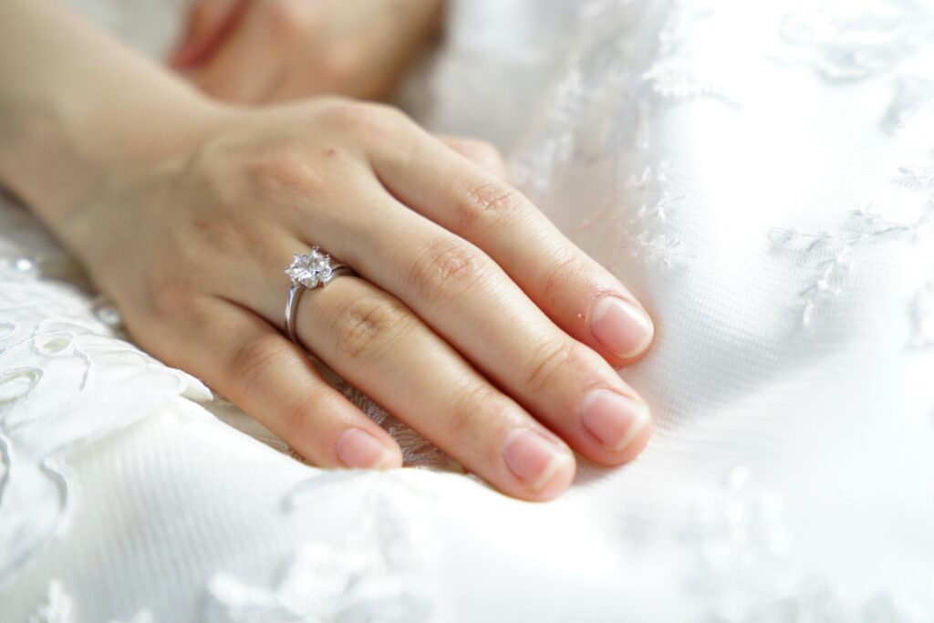 Close-up of a bride's hand with a wedding ring resting on a beautiful white dress.